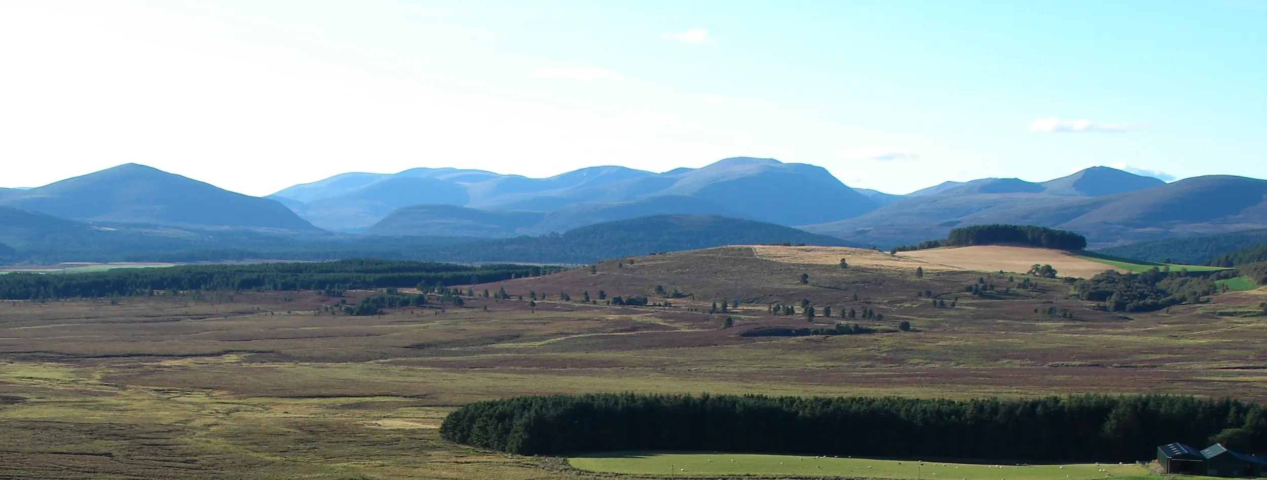 Landscape view across a flat upland landscape leading towards a mountain range which stretches along the horizon.