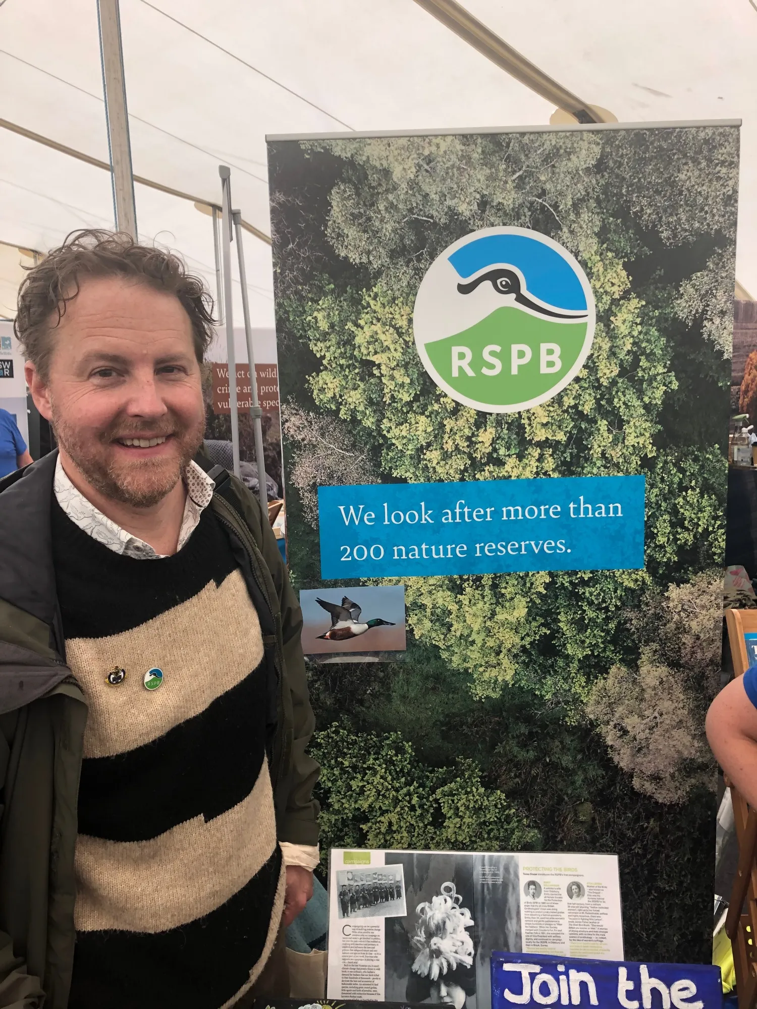 Samuel West stood in front of The PSB stand at Birdfair.